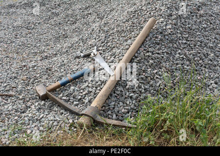 Construction tools: saw, pick and hammer on gravel Stock Photo