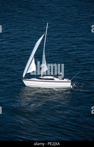 Solo sailor in small sailboat on blue water with reflection of white sails Stock Photo