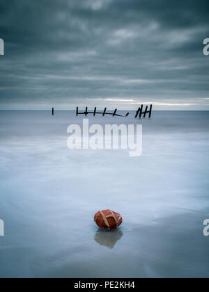 The brick remains of a local house left on the beach with battered sea defences in the background. Stock Photo