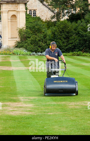 Gardener groundsman cutting mowing the grass lawns at Trinity