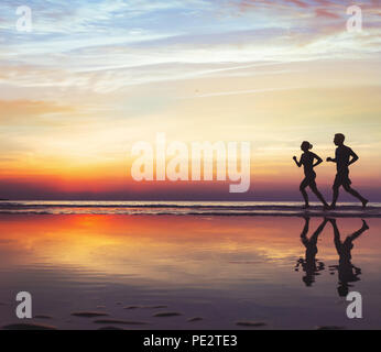 sport and health, two runners on the beach, silhouette of people jogging at sunset, man and woman healthy lifestyle Stock Photo