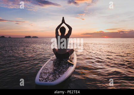 yoga on SUP, silhouette of man sitting in lotus position on stand up paddle board Stock Photo