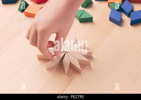 A child plays with colored blocks constructs a model on a light wooden background Stock Photo