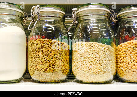 Various raw cereals, grains, beans and pasta for healthy cooking in glass jars on kitchen shelf, white background. Clean eating, vegetarian, vegan, ba Stock Photo