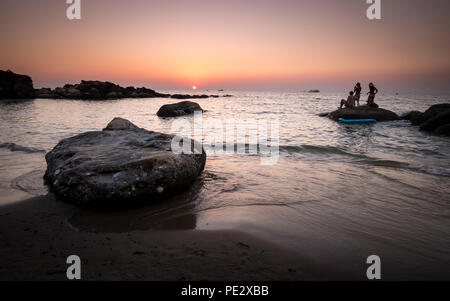 A group of tourists watch the orange sunset from a rock on the island of Phu Quoc, Vietnam Stock Photo