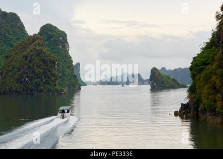 A speedboat heading towards range of islets of Halong Bay, North Vietnam, on a cloudy day. Stock Photo