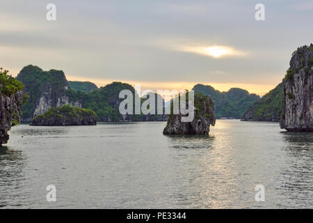 Sunset in Halong Bay, North Vietnam, with sun peaking through overcast sky and rocky islets in the mid ground. Stock Photo