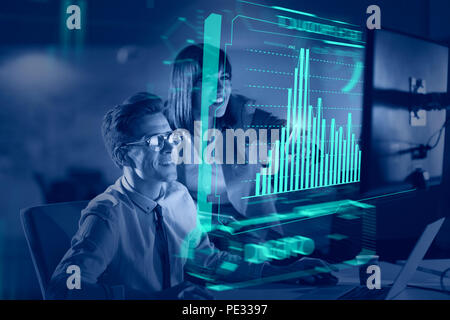 Two young designers are working on a new project in the night office using modern technology with hud display interface Stock Photo