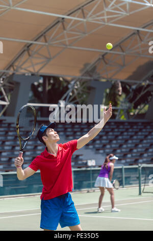 Asian tennis player ready to serve at the beginning of a doubles match Stock Photo
