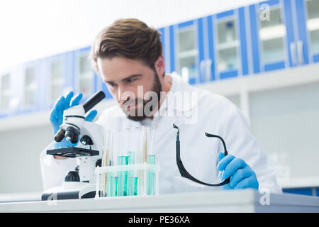 Chemical lab. Selective focus if test tubes standing on the table with a handsome professional chemist working in the background Stock Photo