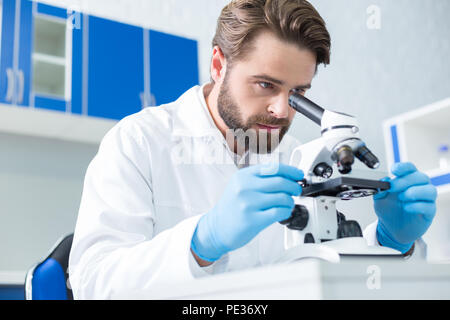 Serious research. Serious nice smart scientist sitting in the lab and focusing on his work while conducting a serious research Stock Photo