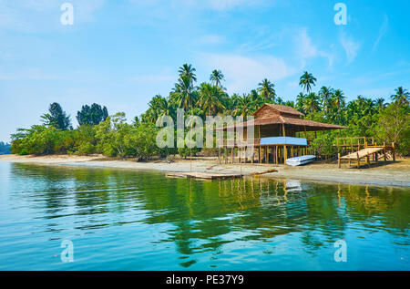 The lush jungle forest and the old wooden stilt house are reflected in waters of the river, Thazin, Ngwesaung, Myanmar. Stock Photo