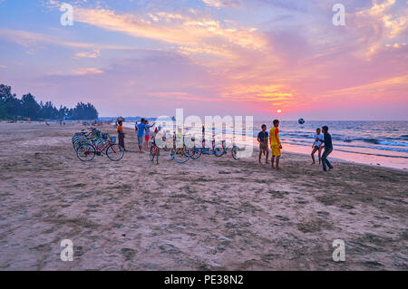 CHAUNG THA, MYANMAR - FEBRUARY 28, 2018: The group of teenagers play chinlone (cane ball) game next to bicycle rental point on the sunset beach of res Stock Photo