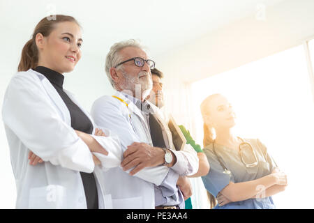 A group of doctors are using a digital tablet for discussing diagnosis and smiling while standing in front of his patient. Stock Photo
