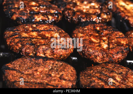 Appetizing hamburgers grilled on the outdoor grill in front of american restaurant. Conceptual picture of finishing cooking a black burger. Hamburger Stock Photo