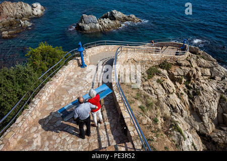 Cliff stone path with stairs to the sea in Lloret de Mar town on Costa Brava in Catalonia, Spain, senior couple tourists looking at map of the town an Stock Photo