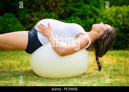 Pregnant Female With Eyes Closed Stretching Back On Yoga Ball Stock Photo