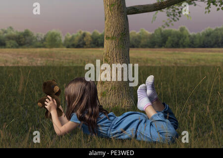 girl laying on grass and playing with fluffy teddy in the meadow field Stock Photo