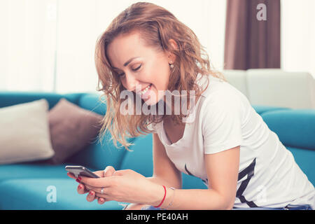 Happy casual girl texting on a mobile phone resting on a couch at home in her cozy apartment Stock Photo