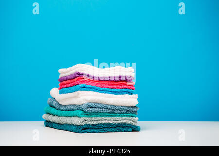 Photo of stacks multi-colored towels on empty blue background. Stock Photo