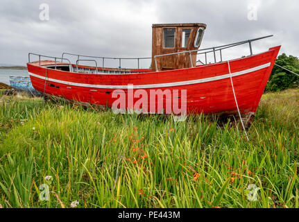 Red fishing boat hauled up out of the water at Roundstone on the coast of Connemara in the west of Ireland Stock Photo