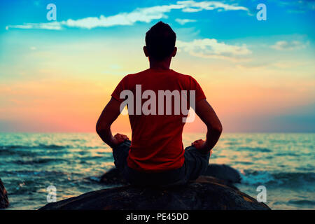 Happy travel tourist practicing yoga pose and meditation on tropical beach at sunset Stock Photo