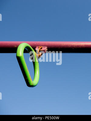 Colour image of a green monkey bar handle on a red pole in a children's playground, shot from below against a clear blue sky Stock Photo