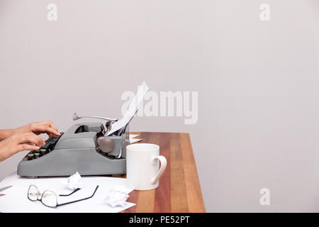 The womans hands typing on an old-fashioned typewriter. On the table are glasses and there is a mug. Neutral background Stock Photo