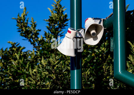Public address bullhorn outdoor speakers on a green post in front of trees Stock Photo