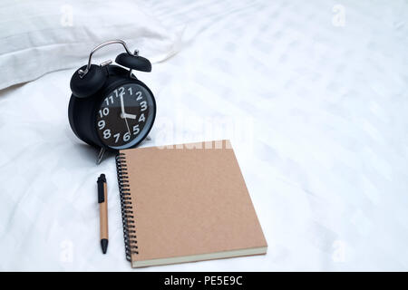 Diary or notebook and vintage alarm clock on bed in bedroom at home or hotel, working or note something before sleep. Stock Photo
