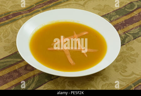 Warm butternut squash soup with carrot in white soup bowl on tablecloth Stock Photo