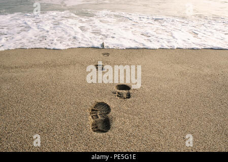 Swallowed in the sea. Shoe footprints in sand. Expressive conceptual imagery. Punta Hermosa, Lima District, Peru. Jul 2018 Stock Photo