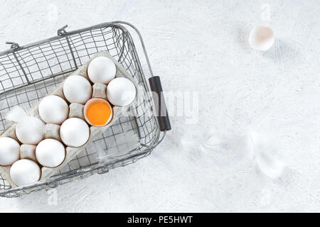 Healthy and organic eggs in white shells, one can see yolk in one. Eggs are in a container and a metal basket, on a white background. Stock Photo