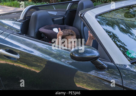 Happy laughing child in a convertible sits in the car child seat and shows the thumbs up. Stock Photo