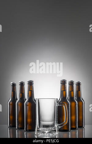 Six beer bottles and big empty cup. Reflections on glossy table. Vertical shot with big copy space to insert your text. Stock Photo