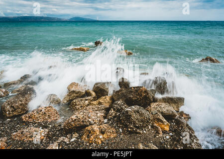 Waves beat against stones on a sunny day in Crete, Greece. Blue Sea Ocean in the background and stone beach in the foreground. Photo taken in Greece. Stock Photo