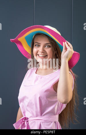 Portrait of beautiful teen girl wearing colorful sun hat against gray background. Stock Photo