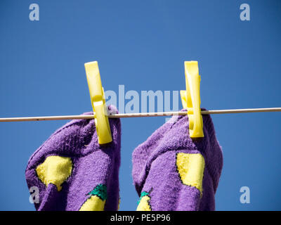 Close up of two purple socks with yellow lemon detail, pegged to a washing line with two yellow clothes pegs, shot from below against a clear blue sky Stock Photo