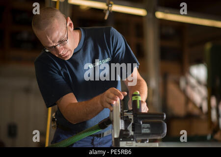 A U.S. Coast Guard damage controlman performs precise triangular cuts on wooden boards at Coast Guard Island in Alameda, California. Part of the damage control shop duties includes carpentry, structural repairs, and maintenance of base systems. These tasks support operational readiness and ensure infrastructure integrity, covering electrical, mechanical, and structural elements. Routine work maintains the functionality of essential base operations and supports Coast Guard mission capabilities. Stock Photo