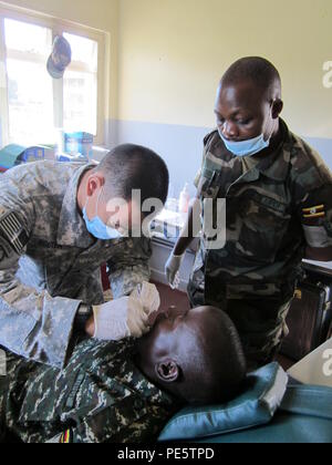 Sgt Nguyen (left), a dental technician, examines the teeth of a Ugandan Peoples Defense Force soldier as UPDF Cpl. Wafula (right), a dental technician observes during Medical Readiness Training Exercise 15-4, Sept. 21, in Jinja, Uganda. USARAF deployed personnel from 44th Medical Brigade and 7th Civil Support Command to Uganda from Sept. 14-25 to set conditions for enhanced readiness of U.S. Army medical professionals, reinforce partnerships with UPDF, and strengthen local health services through expeditionary and field platforms. (U.S. Army photo by 1st Lt. Lorraine Frechette) Stock Photo