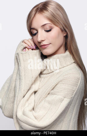 Blonde young beautiful woman dressed in large white cashmere sweater on gray background Stock Photo