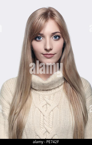 Blonde young beautiful woman dressed in large white cashmere sweater on gray background Stock Photo