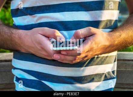 White man holding smart phone in city park outdoors, people using technology Stock Photo