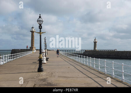 The West Pier at Whitby on the coast of North Yorkshire, England. A man walks along on a sunny spring day. Stock Photo