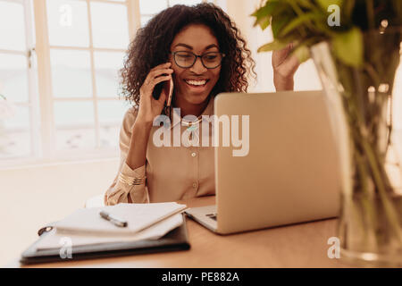 Woman entrepreneur managing her business from home working on laptop computer and discussing business over mobile phone. Businesswoman sitting at home Stock Photo