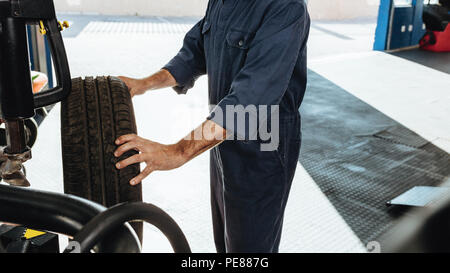 Cropped shot of a mechanic doing car tire checkup on machine in service station. Man inspecting the tire grip in workshop. Stock Photo