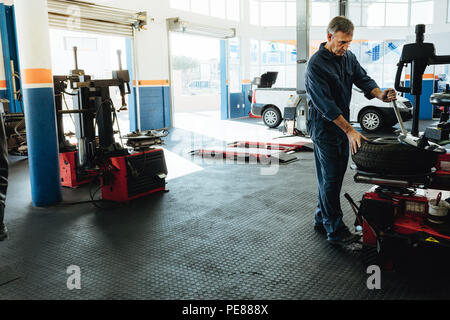 Car service station with mechanic removing tire from disc. Technician working on car tire removing machine in workshop. Stock Photo