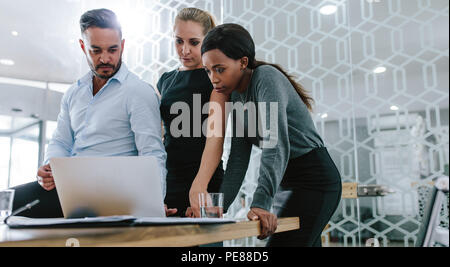 Three diverse business people talking together over a laptop while working at a table in office boardroom. Business team working on their business pro Stock Photo