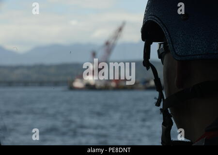 Petty Officer 2nd Class Jeffrey Deck, a boatswain’s mate at the Maritime Force Protection Unit in Bangor, Wash., looks out at a barge with a crane working along the Hood Canal Bridge prior to passing through the bridge exercise Northern Vindicator, Sept. 23, 2015. A 1,000-yard safety zone was in effect during the exercise, which included boat tactics, security zone maintenance and weapons capabilities, utilized to improve the qualifications of personnel charged with protecting the community, maritime environment and other naval vessels. (U.S. Coast Guard photo by Petty Officer 3rd Class Amanda Stock Photo