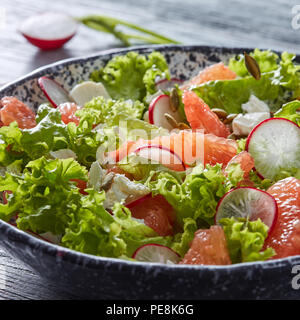 Freshly prepared dietary vegetarian salad with natural organic vegetables, citrus fruits, in a black plate on a gray wooden table. Stock Photo